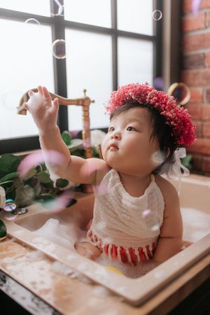 A baby in a white dress with red pom-pom hair accessories sits at a table in multiple sequential photos在多張連續的照片中，一個穿著白色連身裙、頭戴紅色絨球髮飾的嬰兒坐​​在桌旁