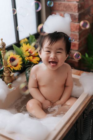 Happy baby enjoying bathtime with bubbles and sunflowers in a vintage-style bathtub setting.快樂的寶寶在復古風格的浴缸裡享受著泡泡和向日葵帶來的沐浴時光。