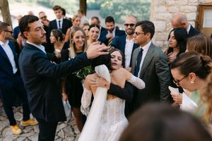 Joyful wedding guests celebrating with bride in lace gown at rustic outdoor Italian ceremony.