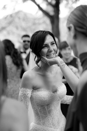Smiling bride in lace off-shoulder wedding dress with veil at outdoor ceremony.