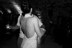 Black and white photo of bride in backless wedding dress dancing at reception in rustic stone venue.