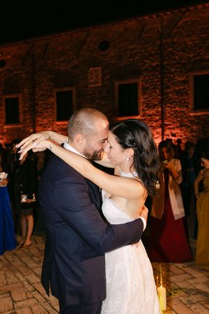 Bride and groom share an intimate first dance embrace at an outdoor evening wedding reception at a historic stone venue.