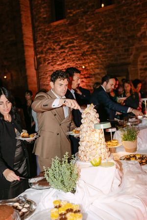 Guest serves himself at elegant wedding dessert table featuring croquembouche tower and assorted pastries.