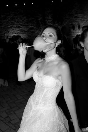 Black and white photo of bride in lace gown playfully blowing a bubble at a wedding reception.