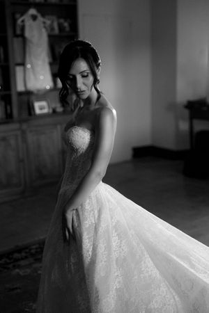 Black and white photo of a bride in a strapless lace wedding gown gazing down in a softly lit room.