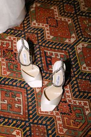 Jimmy Choo bridal heels with crystal embellishments displayed on colorful geometric patterned rug.