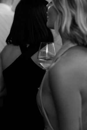 Black and white photo of two women in elegant dresses holding a wine glass at a wedding reception.