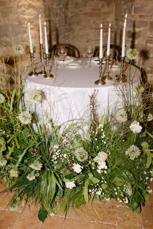 Elegant wedding sweetheart table with white candles, silver candlesticks, and lush wildflower greenery arrangements.