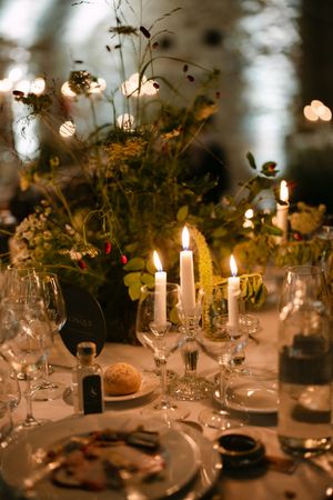 Candlelit wedding reception table with wildflower centerpiece, crystal glassware, and warm ambient lighting.