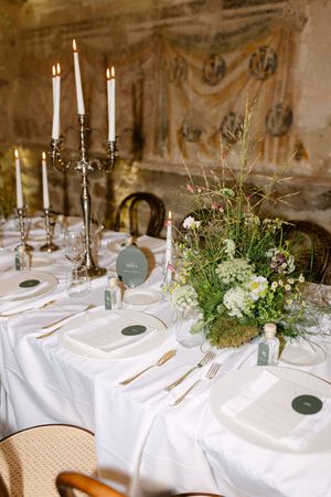 Romantic wedding reception table with silver candelabras, wildflower centerpieces, white linens, and gold place settings.