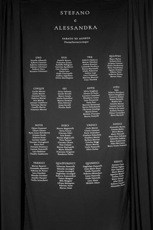 Wedding seating chart for Stefano e Alessandra displayed on dark draped backdrop.