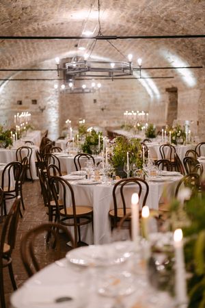 Romantic candlelit wedding reception in a rustic stone vaulted cellar with round tables.