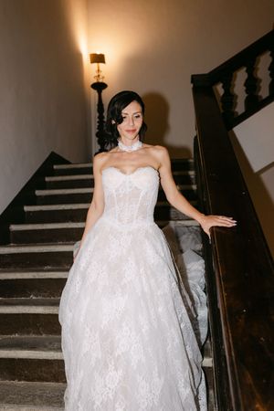 Elegant bride in a strapless lace ballgown poses gracefully on a grand staircase in warm light.