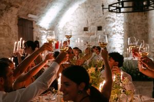 Wedding guests raising glasses in a candlelit toast inside a rustic stone-walled reception venue.