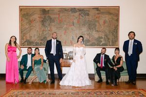 Wedding party posing before ornate tapestry in elegant venue with colorful attire.