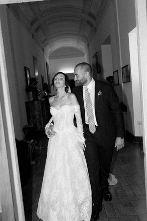 Elegant bride and groom walking through arched hallway in black and white photo.