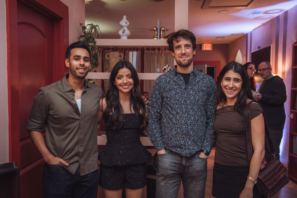 Four friends smiling and posing together at an indoor party event with warm ambient lighting.