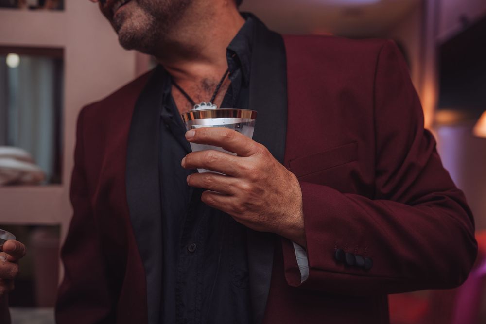 Elegant man in red blazer holding a cocktail glass at a sophisticated evening event.