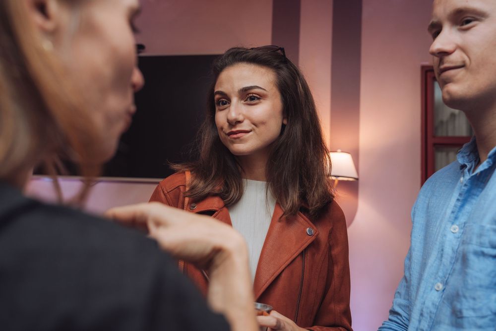 Young woman in red jacket smiling during a social gathering conversation indoors.