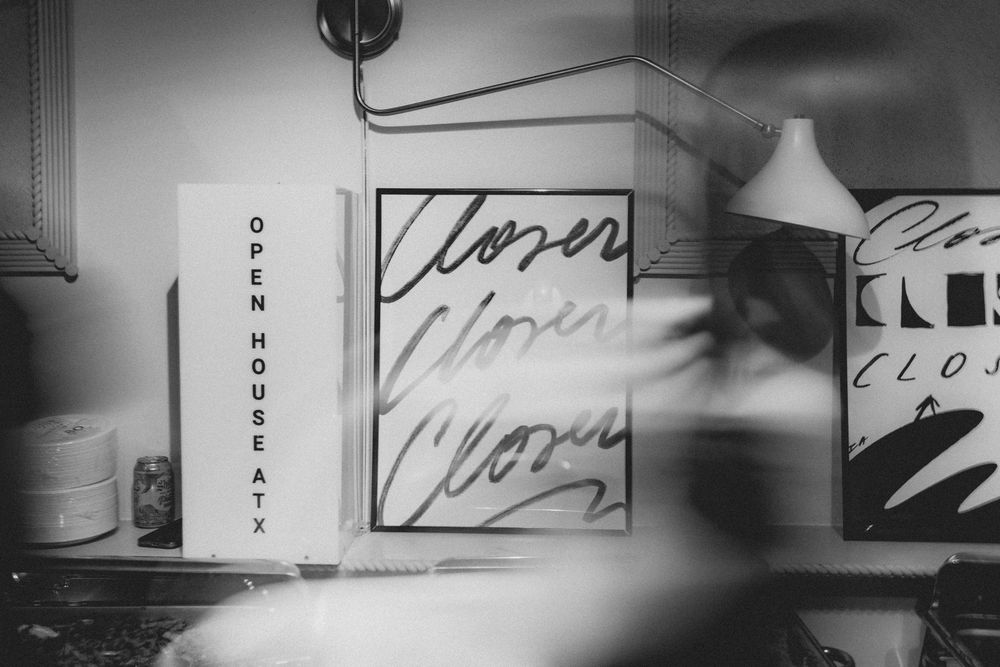 Black and white photo of an Open House sign next to Closed signs in a shop window display.