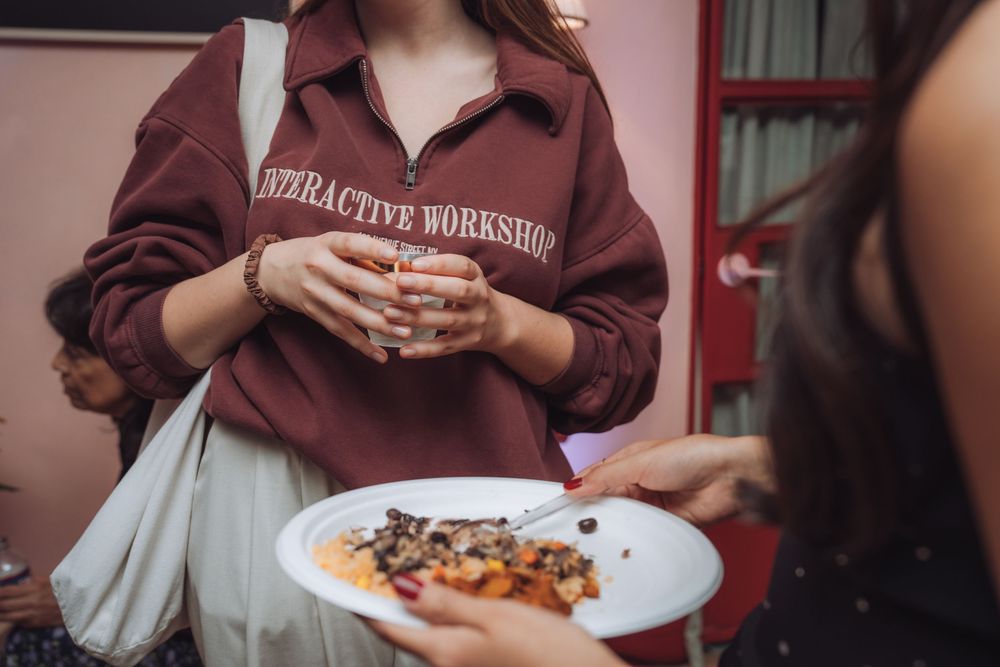Person wearing Interactive Workshop sweatshirt holding food plate at casual event.