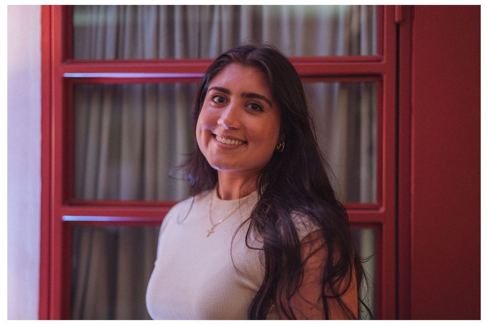Young woman smiling warmly, leaning against a red wooden door frame in a cozy indoor setting.