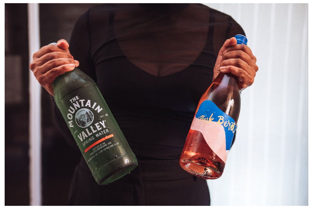 Person holding Mountain Valley spring water bottle and pink rosé wine bottle in both hands.