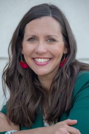 Smiling brunette woman with red earrings in green top, professional headshot portrait.