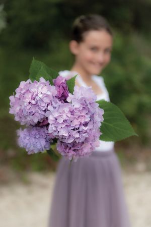 Close-up of purple hydrangea bouquet held by girl in lavender tulle skirt outdoors.