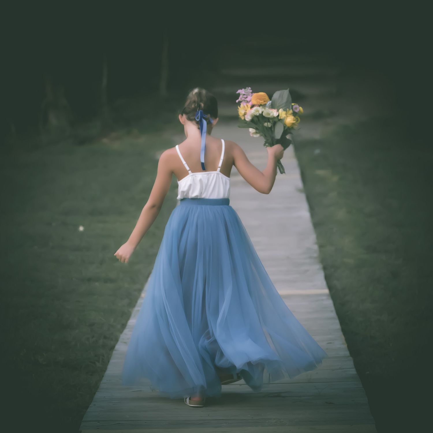 A young girl in a blue tulle skirt walks down a path holding a bouquet of colorful flowers.