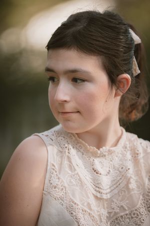 Close-up portrait of young girl in lace dress with hair accessory, soft natural light.