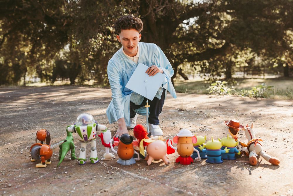 Young man arranging Toy Story character figurines including Buzz Lightyear and Woody on a park path outdoors.