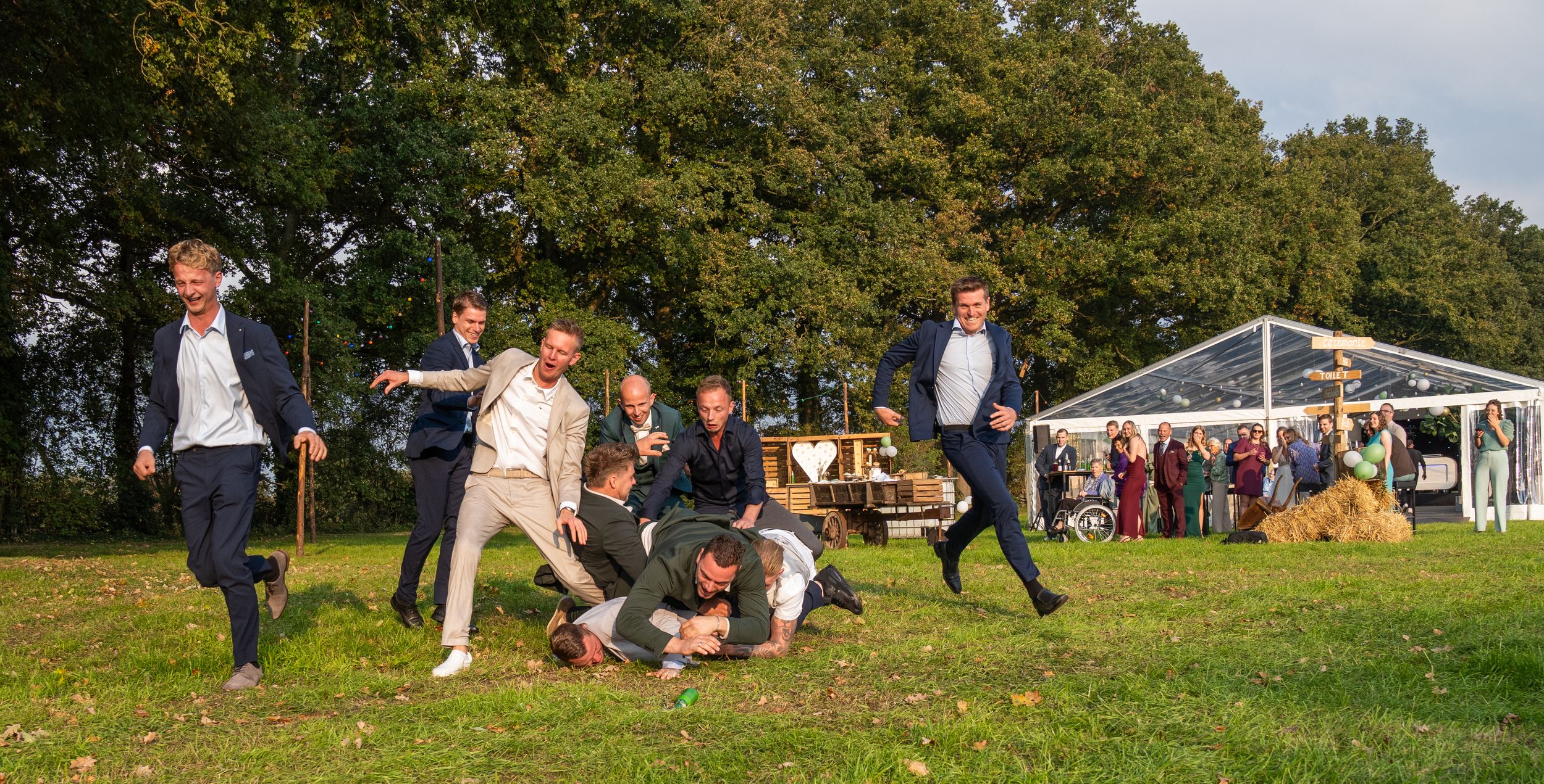 Bruiloftsgasten spelen een levendig buitenspel op een zonnige dag in de buurt van een witte tent.