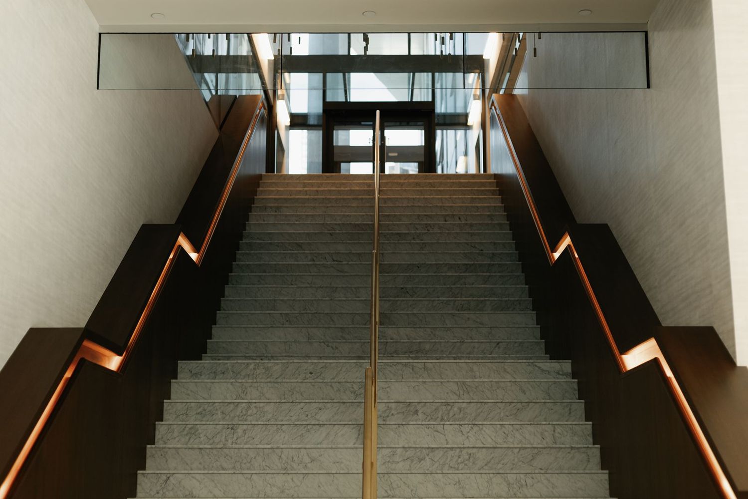 Modern venue staircase with granite steps and copper handrails leading to glass doors.