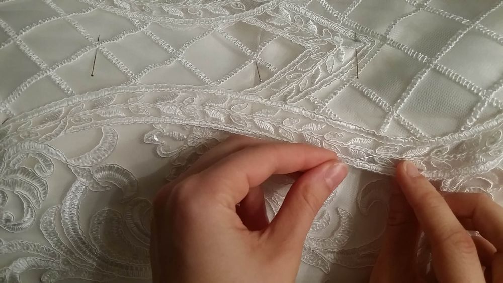 Nahaufnahme von zwei Händen die ein Brautkleid nähen