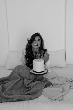 A series of black and white boudoir photos showing a person lying on white bedding while wearing a gray sweater.