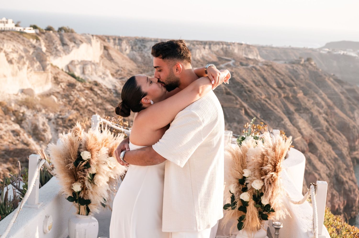Couple embracing at outdoor wedding ceremony with mountain backdrop and floral arrangements.