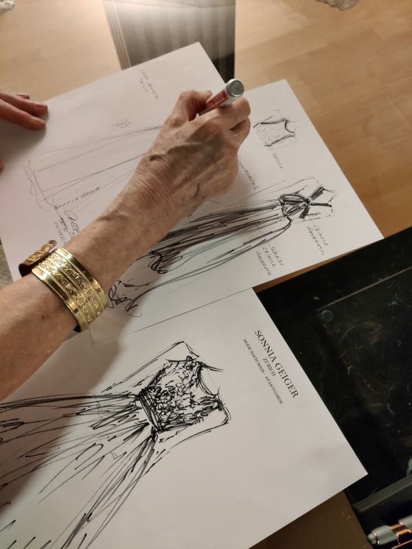 Eine Hand zeichnet ein Kleid auf Papier.