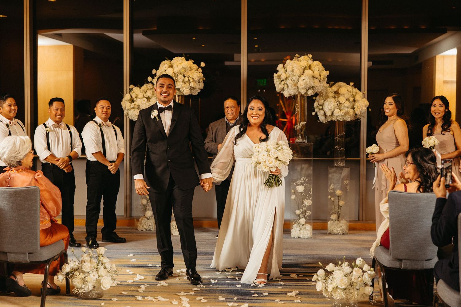 Wedding party lineup with bridesmaids in white dresses and groomsmen in formal attire.