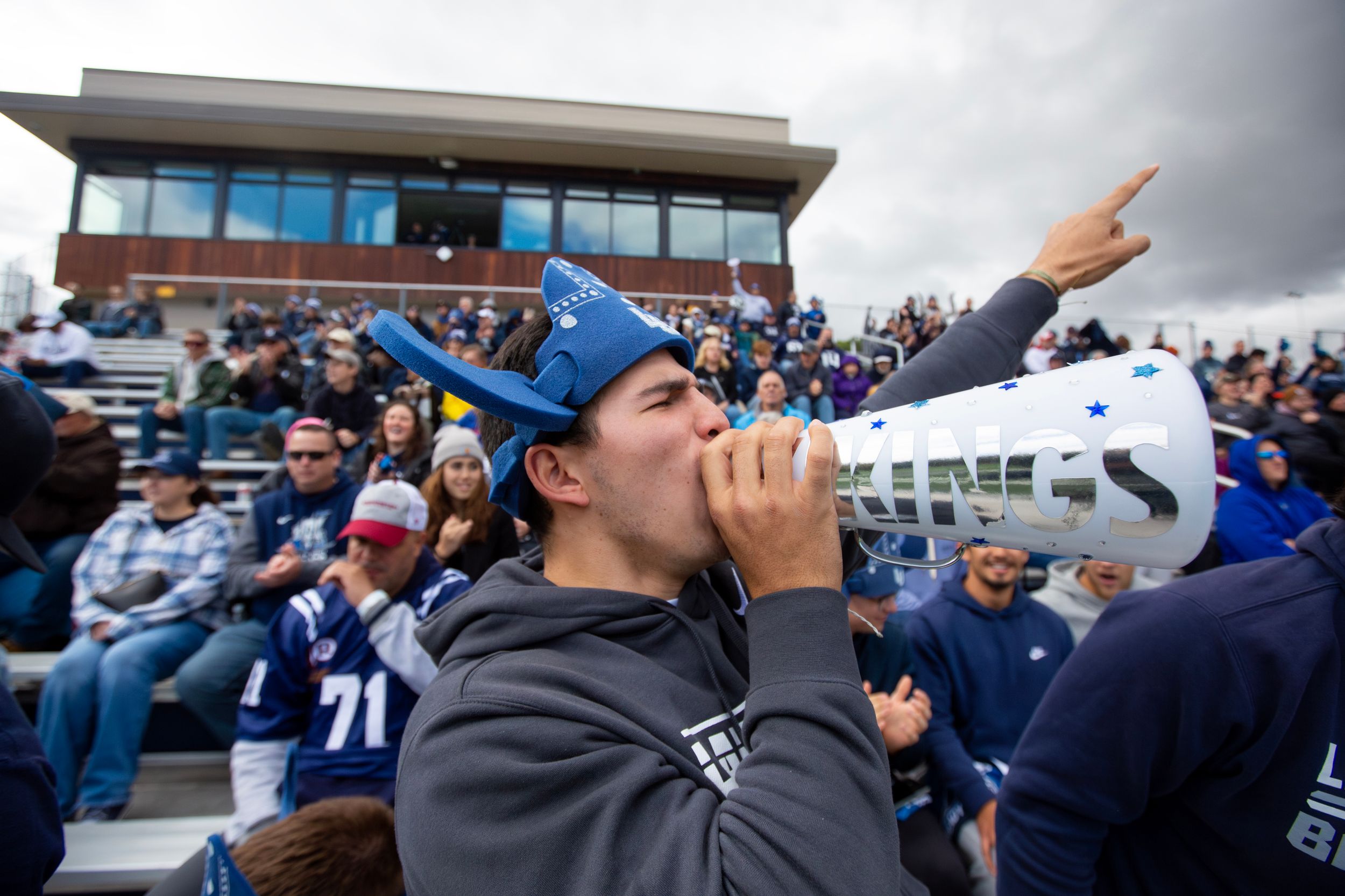 A football fan holds a megaphone and cheers in the stands.