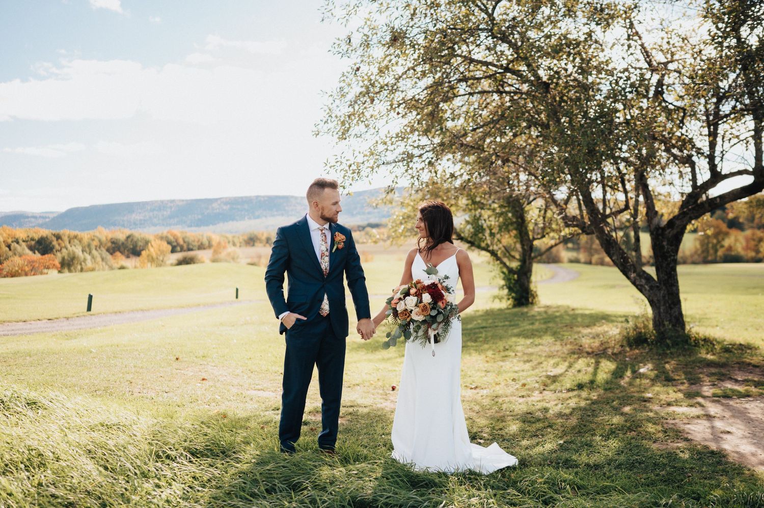 Bride and groom holding hands in a colorful autumn landscape on a scenic golf course wedding day.