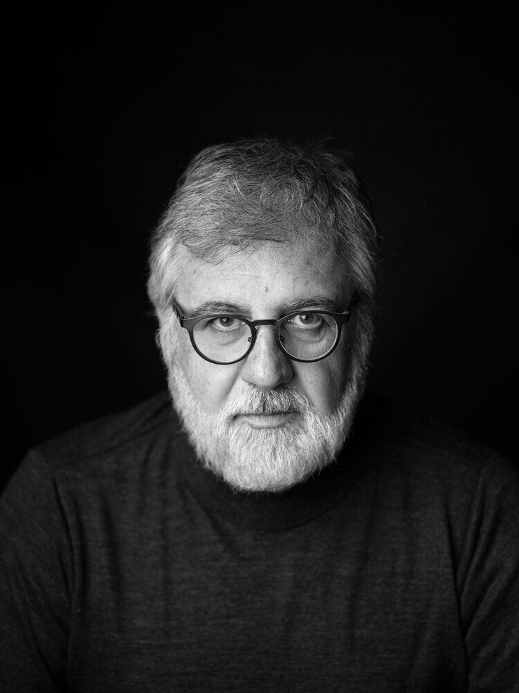 Dramatic black and white portrait of a figure in glasses with a white beard.