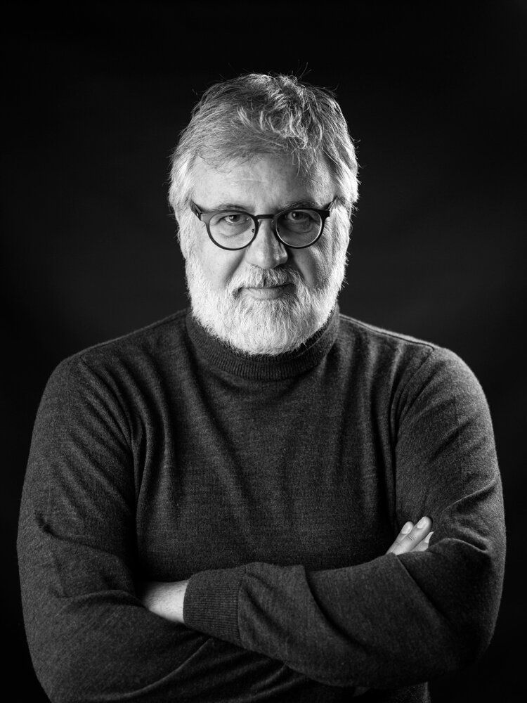 Black and white portrait of someone with crossed arms wearing a dark sweater and glasses.