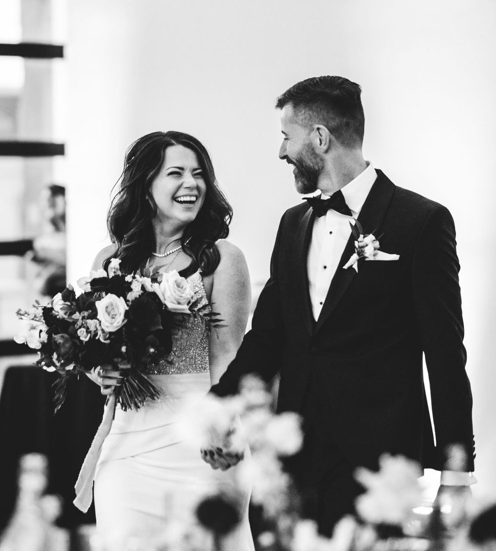 Wedding couple sharing joyful moment in formal attire with bridal bouquet.