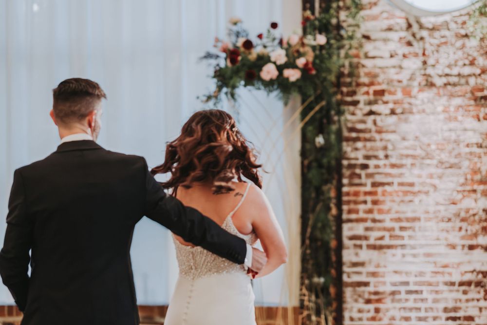 Back view of a couple dancing in an elegant brick-walled venue with floral decor.