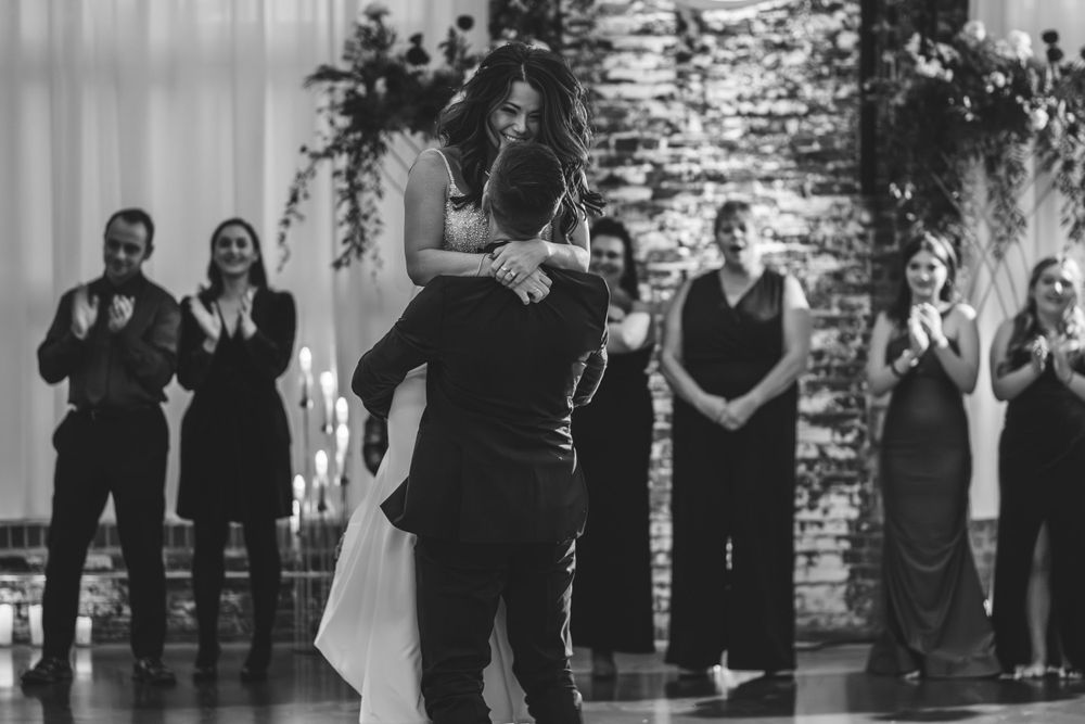 Black and white photo of couple dancing at wedding reception with guests applauding.