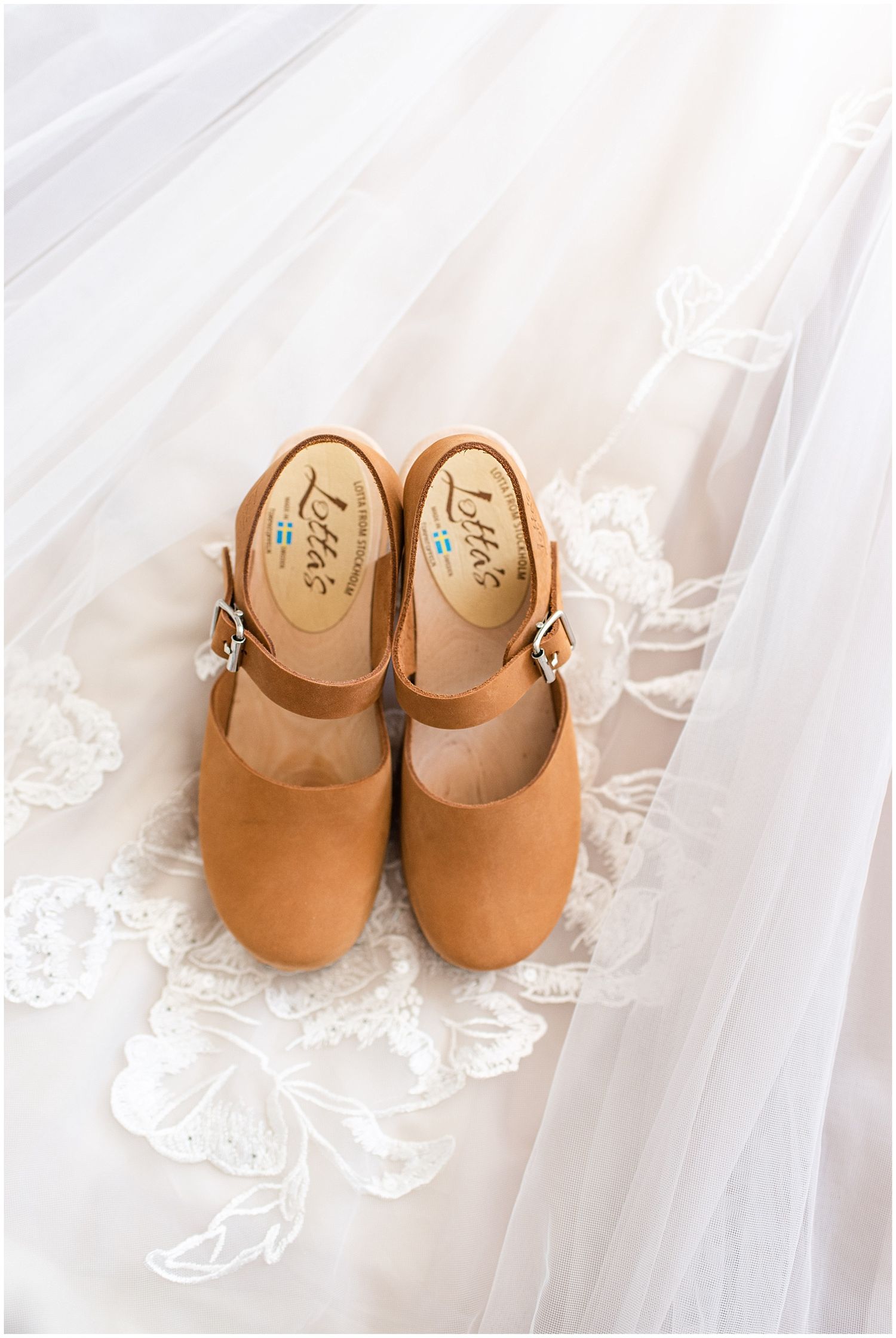Tan leather Mary Jane clogs with buckle straps displayed on a white lace bridal veil.