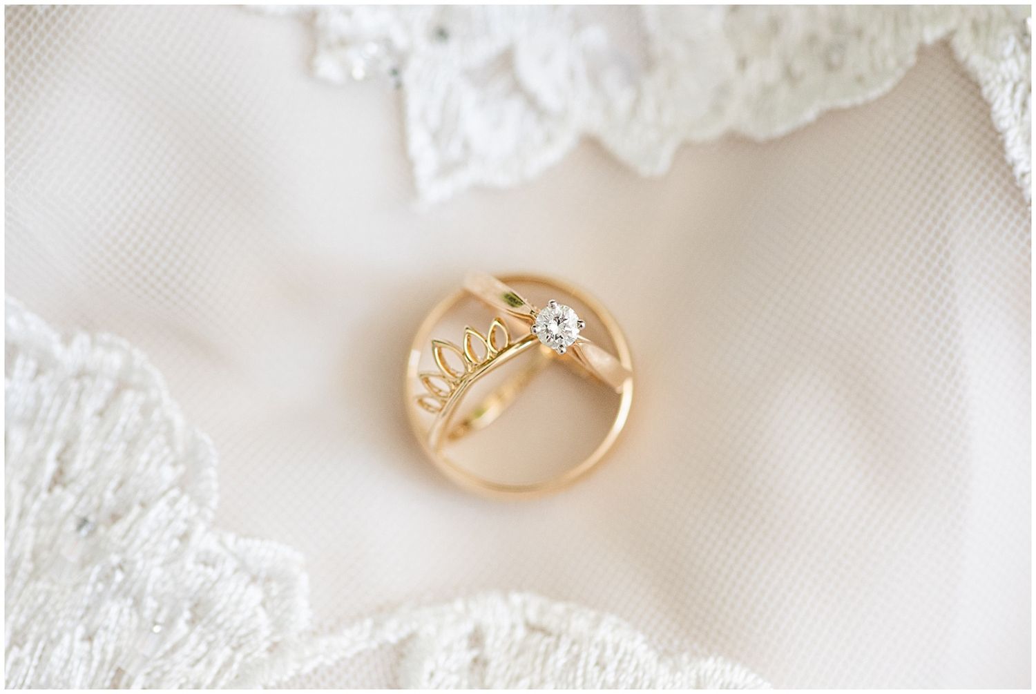 Gold wedding band with diamond solitaire engagement ring displayed on white lace bridal fabric.