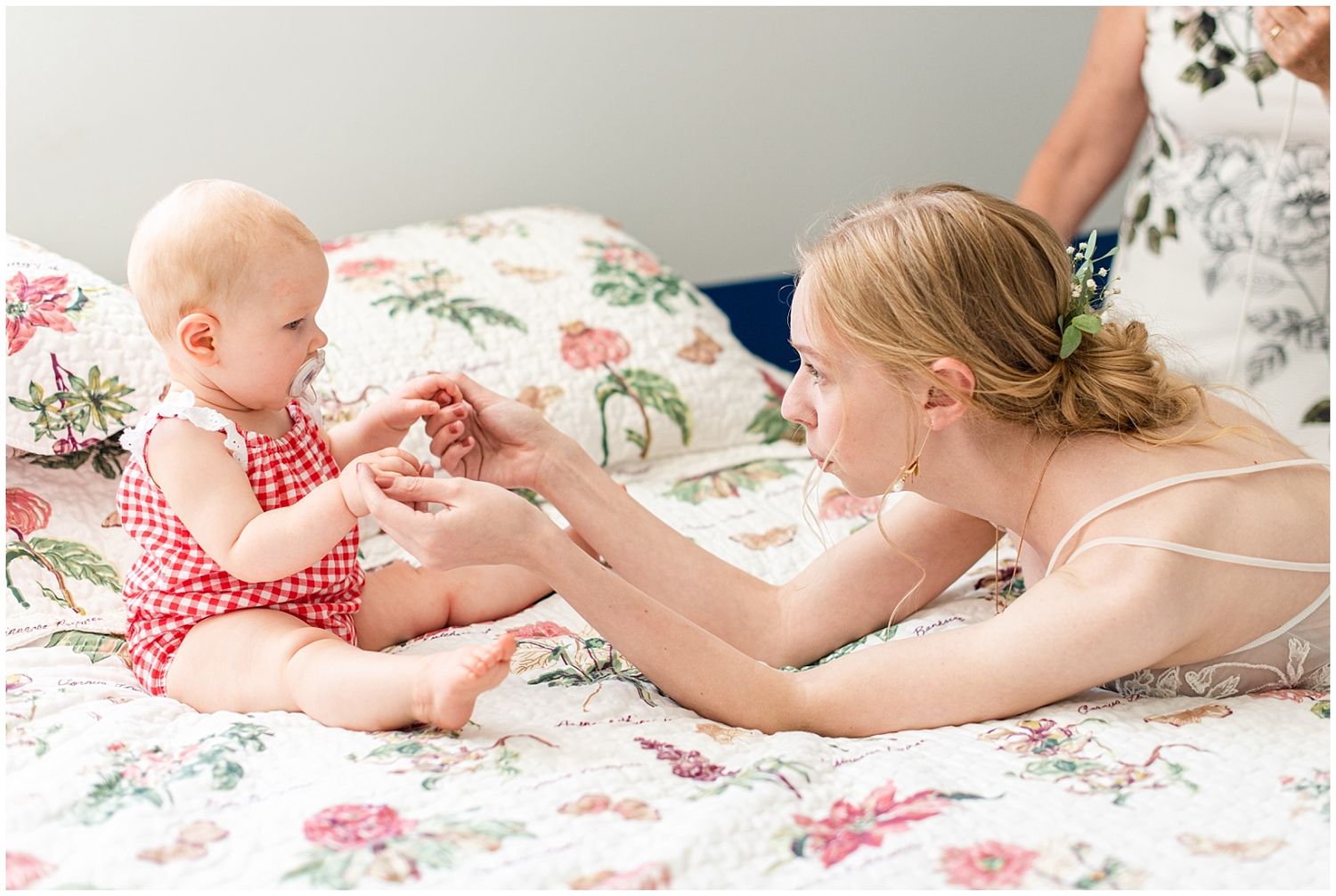 A mother tenderly interacts with her baby on a floral quilt, sharing a sweet bonding moment together.