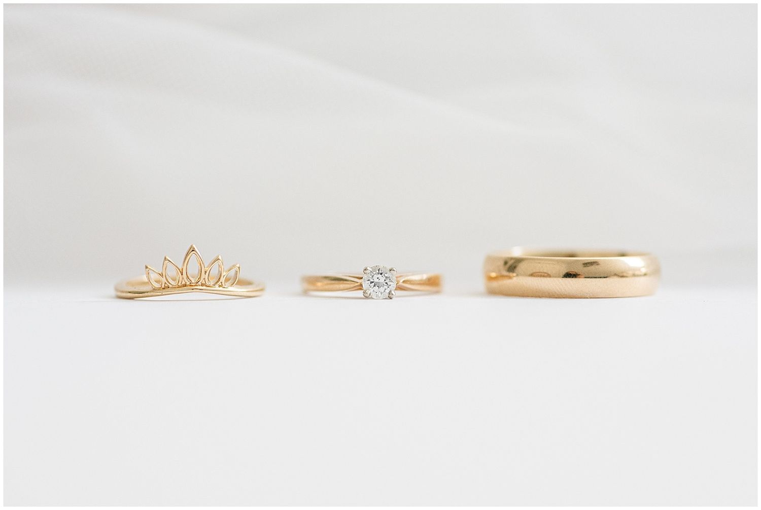 Three gold wedding rings displayed on white surface including a crown ring, solitaire diamond, and band.